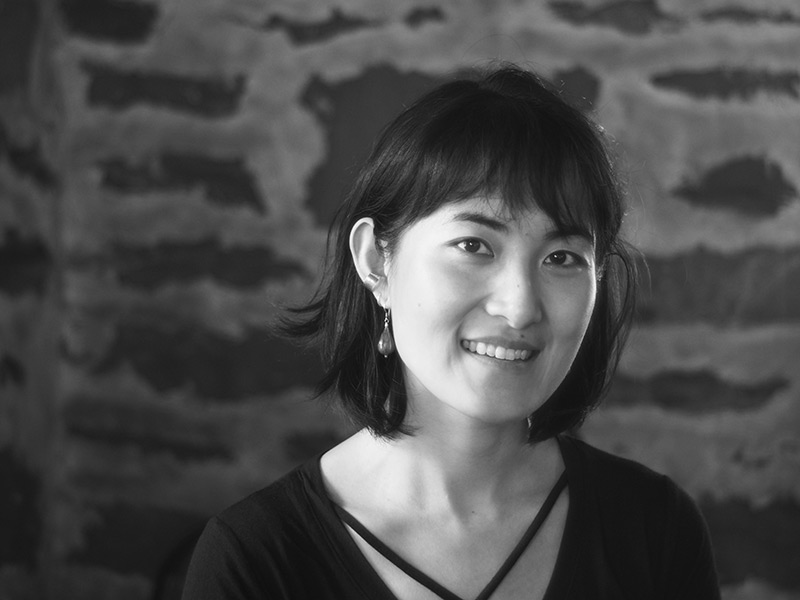 Black and white portrait of Natasha Lin, She has black hair, tear drop earrings and a great smile. Wearing a dark vneck blouse. 