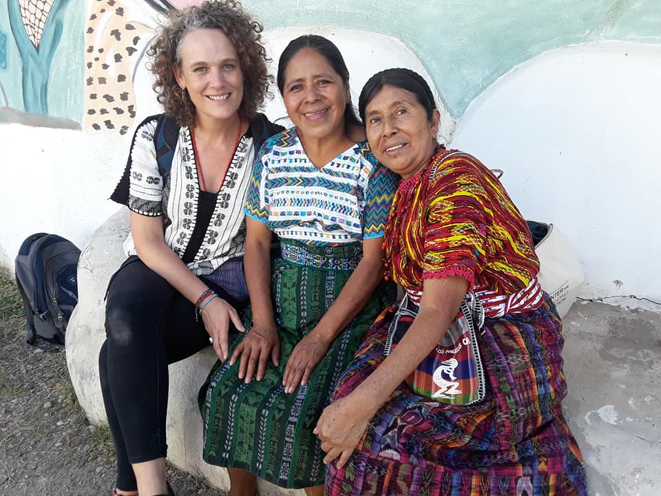 Three adult women pose together in a seated position on a stone stoop.